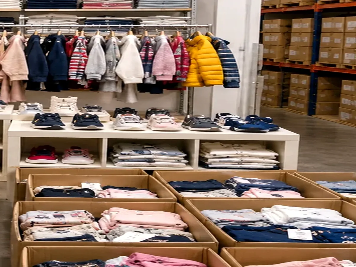 Logistica per ritiro stock abbigliamento bambino con pallet scatole e capi moda in magazzino luminoso